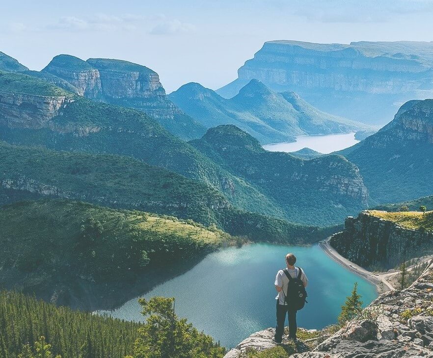 A person standing on a cliff looking at a view of water and mountains.